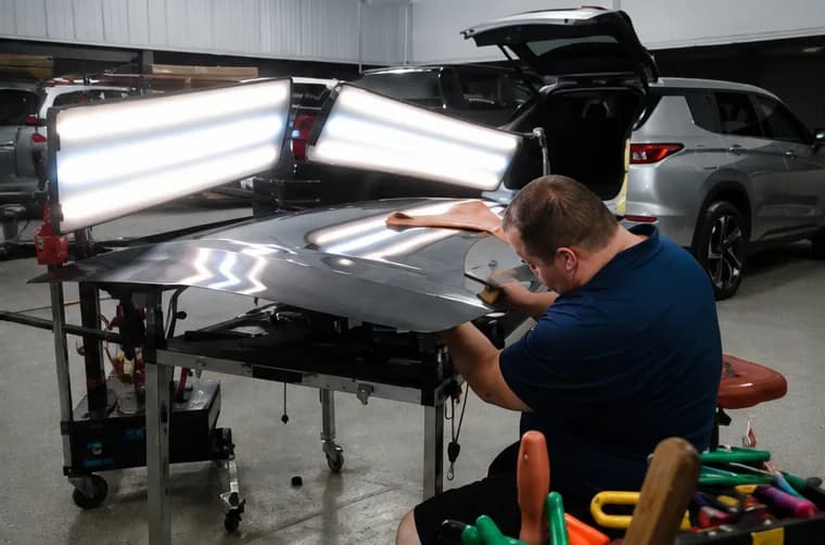 Technician reading hail dents on a hood under paintless dent repair lights